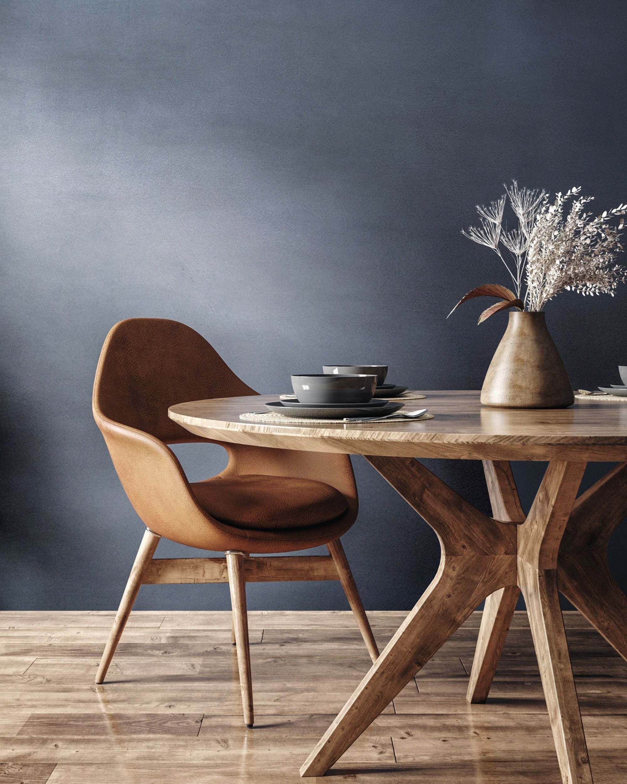 Stylish dining area featuring a brown chair, wooden table, and decorative vase with dried flowers against a blue wall.