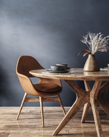 Stylish dining area featuring a brown chair, wooden table, and decorative vase with dried flowers against a blue wall.