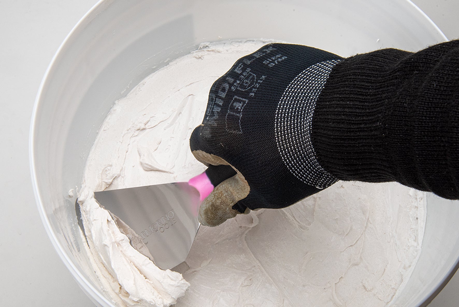 Hand using Venice Bucket Spatola 80mm to scoop mikrosement from a white bucket.